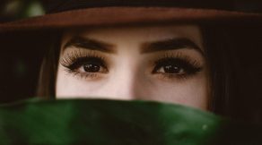 A girl with a hat and wearing eyelash and covering herself with someting green.